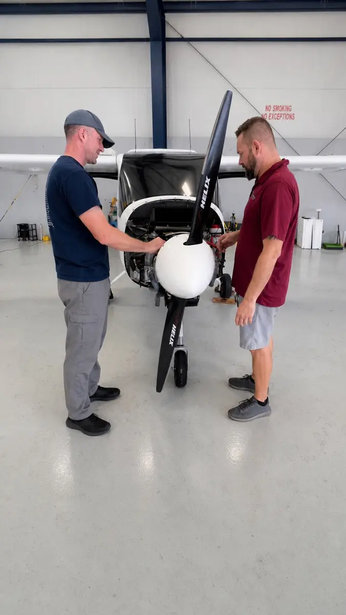 Two people inspecting a light aircraft propeller in a hangar